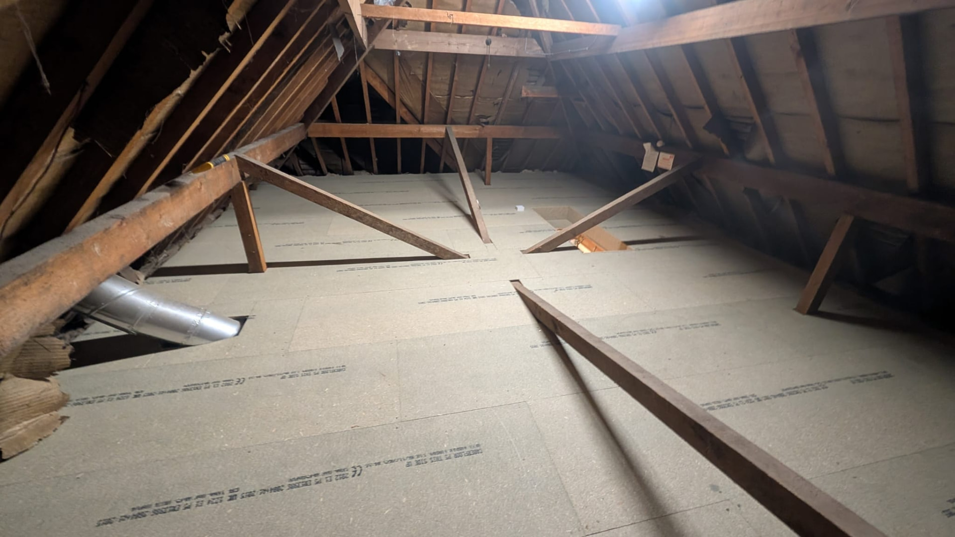 Loft after boarding, clean boarded storage deck fitted neatly around trusses and pipework