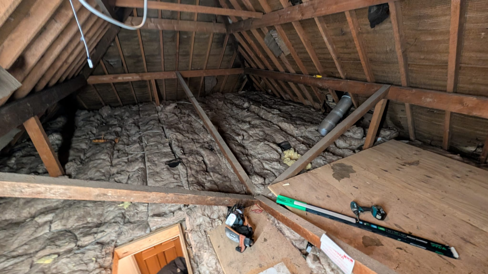 Loft before boarding, flattened, discoloured insulation and a single plywood offcut for storage